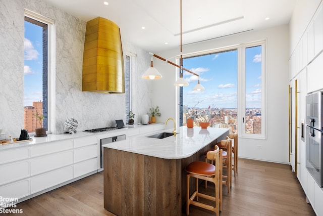 kitchen featuring a sink, light wood-style flooring, white cabinets, stainless steel gas stovetop, and light stone counters