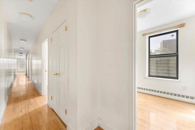 hall with light wood finished floors, a baseboard heating unit, and baseboards