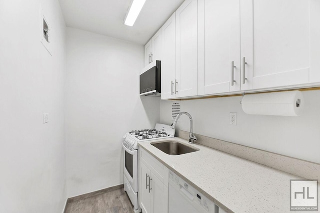 kitchen with white appliances, a sink, white cabinetry, light stone countertops, and light wood finished floors