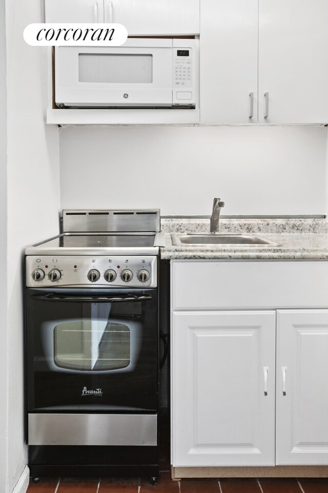 140 W 69th St Unit 124A, New York City, NY 10023 - kitchen featuring electric range, white microwave, a sink, and white cabinetry