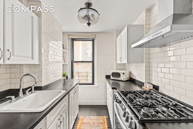 70 E 96th St Unit 2D, New York City, NY 10128 - kitchen featuring wall chimney range hood, a sink, stainless steel range with gas stovetop, dark countertops, and white cabinets