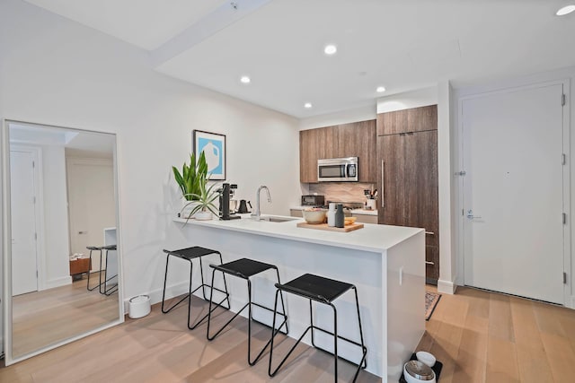 kitchen with stainless steel microwave, a breakfast bar area, light wood-style flooring, a peninsula, and modern cabinets