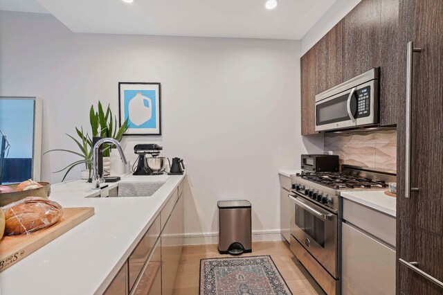 kitchen with stainless steel appliances, a sink, backsplash, recessed lighting, and light countertops