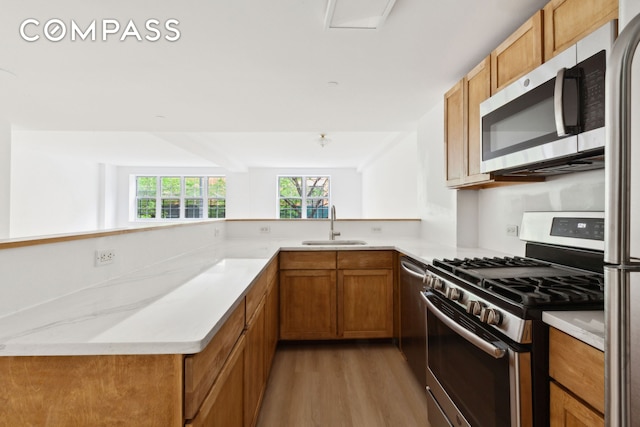 kitchen featuring stainless steel appliances, light wood-type flooring, brown cabinetry, a sink, and a peninsula