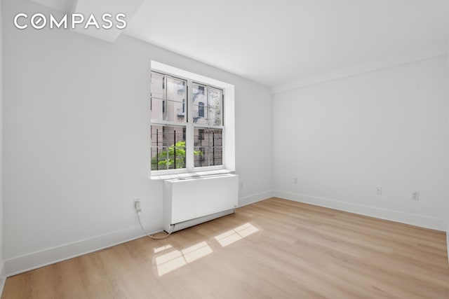 spare room featuring light wood-style flooring, baseboards, and radiator heating unit