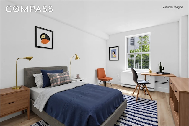 bedroom featuring a baseboard heating unit, light wood-type flooring, and an office area