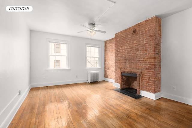 unfurnished living room featuring radiator heating unit, a fireplace, wood-type flooring, a ceiling fan, and baseboards