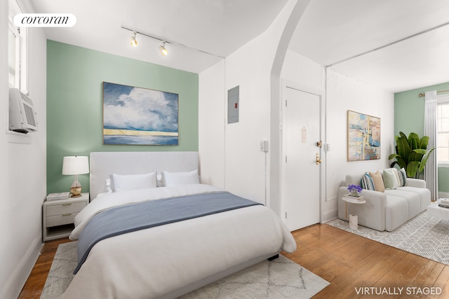 bedroom with wood finished floors, arched walkways, and rail lighting