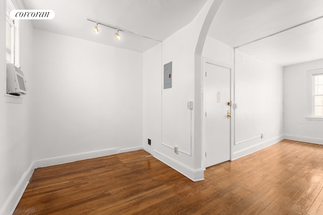 empty room featuring arched walkways, hardwood / wood-style flooring, rail lighting, baseboards, and electric panel