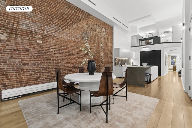 dining space featuring a high ceiling, baseboard heating, light wood-style floors, and brick wall