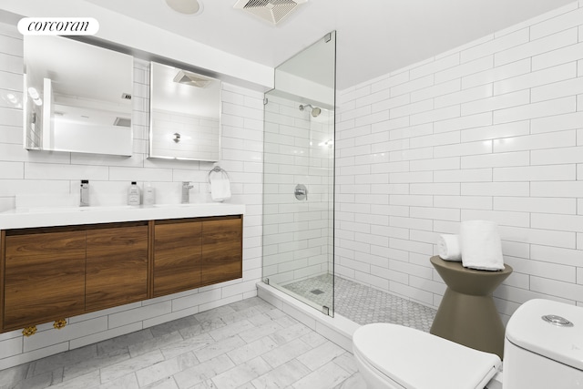 full bath featuring toilet, tile walls, a tile shower, and double vanity