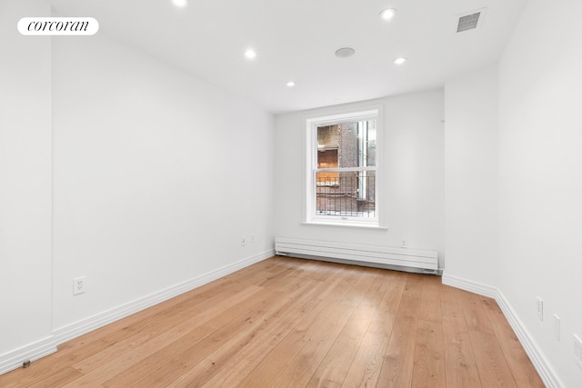 empty room featuring a baseboard heating unit, light wood-type flooring, recessed lighting, and baseboards