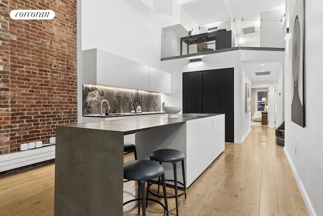 kitchen with a towering ceiling, light wood-type flooring, a breakfast bar, a sink, and baseboards