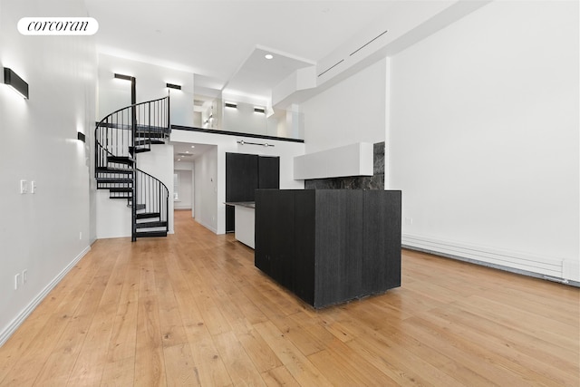 kitchen featuring dark cabinets, light wood finished floors, a towering ceiling, baseboards, and recessed lighting