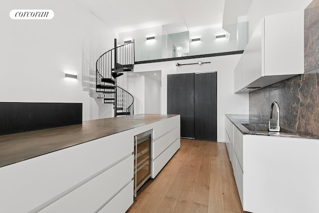 kitchen with wine cooler, white cabinetry, modern cabinets, a sink, and light wood-style flooring