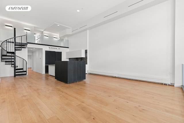 spare room featuring light wood finished floors, stairs, a towering ceiling, and a baseboard heating unit