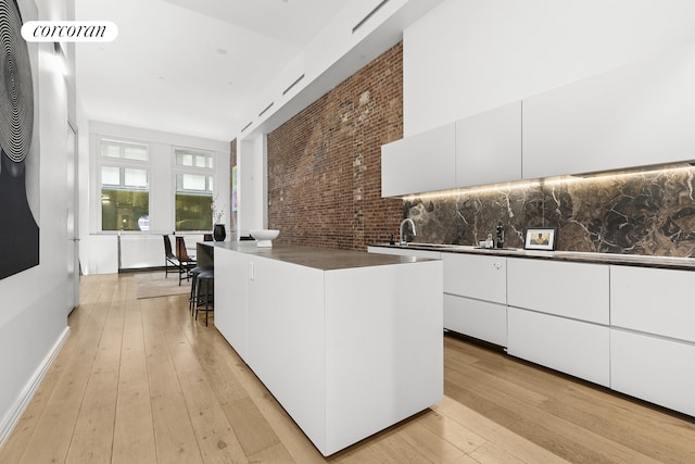 kitchen with modern cabinets, dark countertops, white cabinetry, light wood-style floors, and brick wall