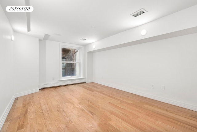empty room featuring light wood-type flooring, a baseboard radiator, and baseboards