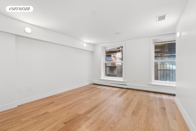 spare room with a baseboard radiator, light wood finished floors, and baseboards