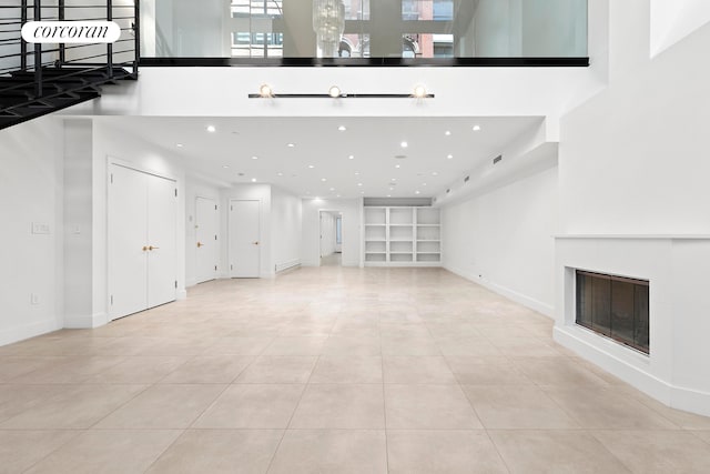 unfurnished living room with built in shelves, light tile patterned flooring, a glass covered fireplace, recessed lighting, and baseboards