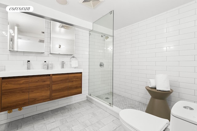 full bath with toilet, tile walls, a tile shower, double vanity, and marble look tile flooring