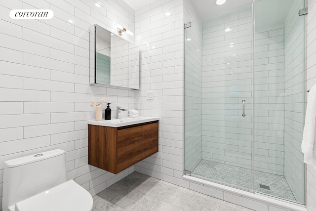 bathroom with tile walls, a shower stall, toilet, and vanity