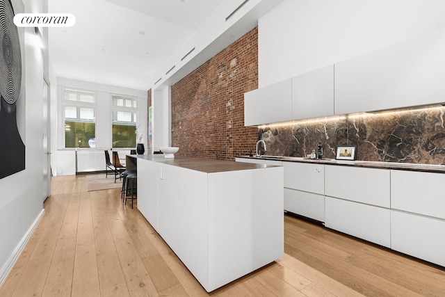 kitchen with dark countertops, modern cabinets, white cabinets, light wood-style floors, and brick wall