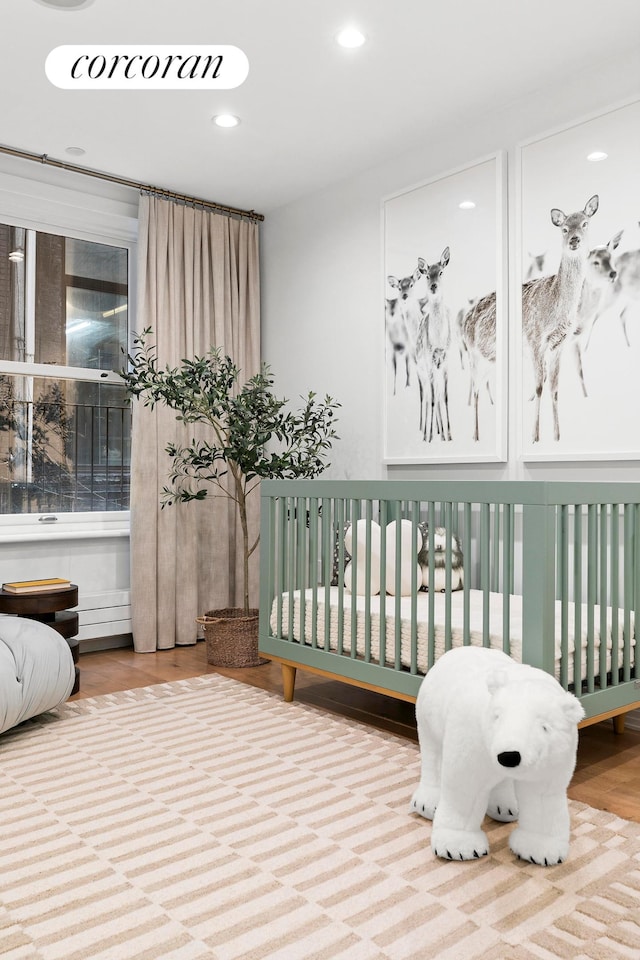 bedroom with recessed lighting, a nursery area, and wood finished floors