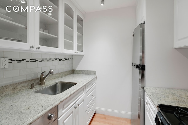 kitchen featuring a sink, backsplash, glass insert cabinets, appliances with stainless steel finishes, and white cabinets