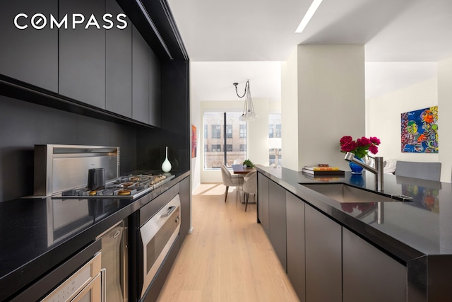 kitchen with a sink, dark countertops, light wood-type flooring, and stainless steel gas cooktop