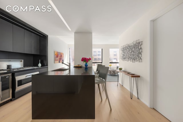kitchen with a sink, oven, light wood finished floors, stainless steel gas stovetop, and beverage cooler