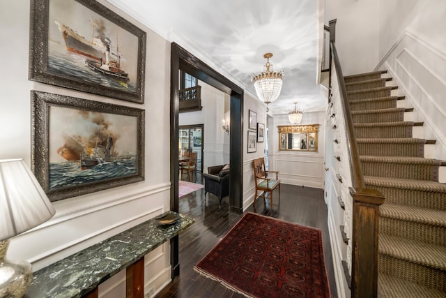 hallway featuring a chandelier, dark wood-type flooring, stairway, wainscoting, and a decorative wall