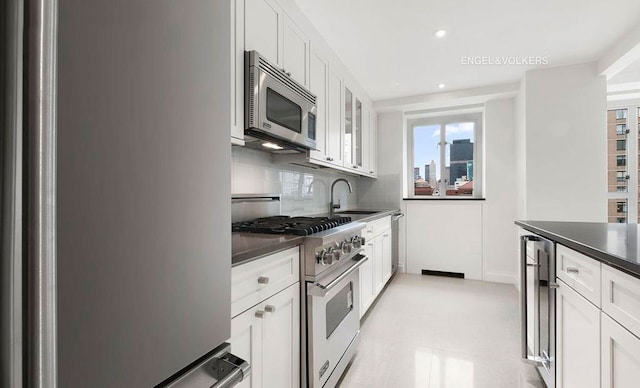 200 E 66th St Unit C1605, New York City, NY 10065 - kitchen featuring appliances with stainless steel finishes, a sink, dark countertops, white cabinetry, and glass insert cabinets