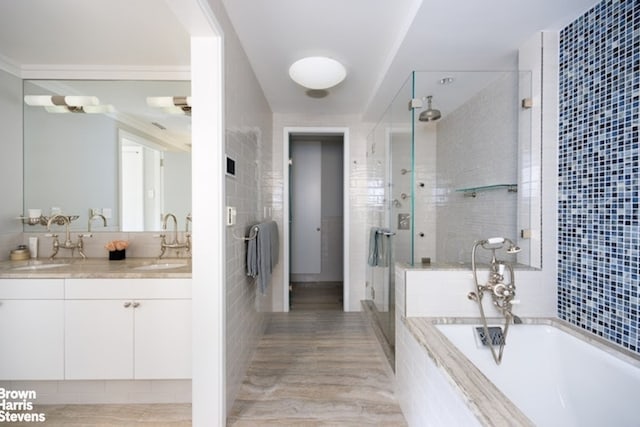 bathroom with tile walls, a stall shower, a bath, double vanity, and wood finished floors