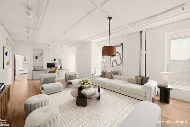 living area featuring wood finished floors, an AC wall unit, built in shelves, and rail lighting