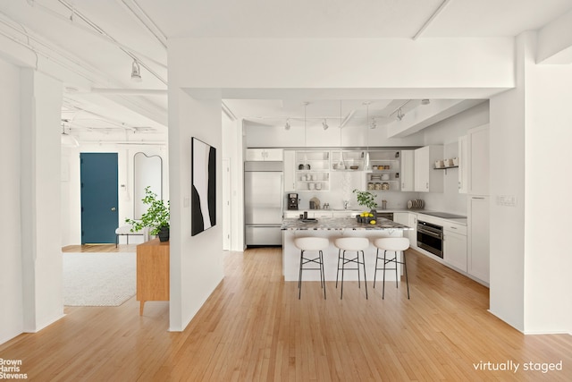 kitchen with rail lighting, built in refrigerator, open shelves, oven, and a breakfast bar