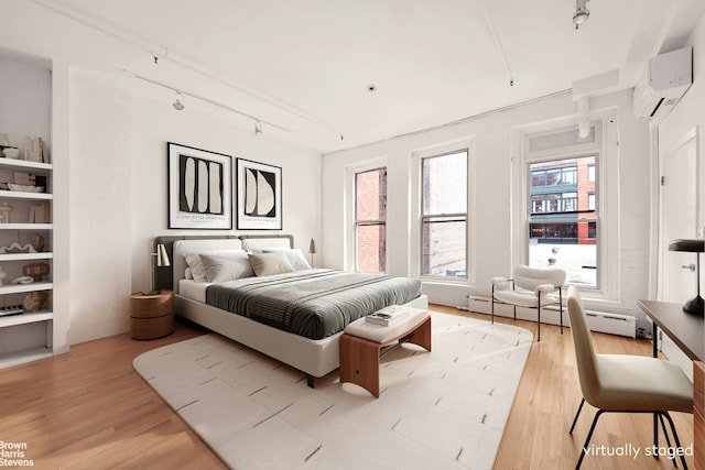 bedroom with track lighting, a wall mounted air conditioner, light wood finished floors, and baseboard heating