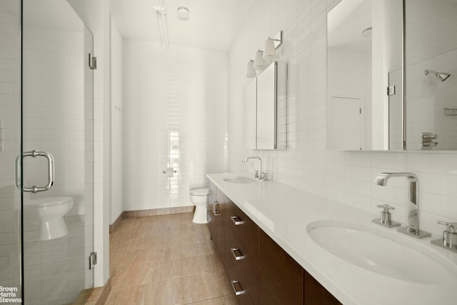 bathroom featuring toilet, tile patterned flooring, a shower stall, double vanity, and tile walls