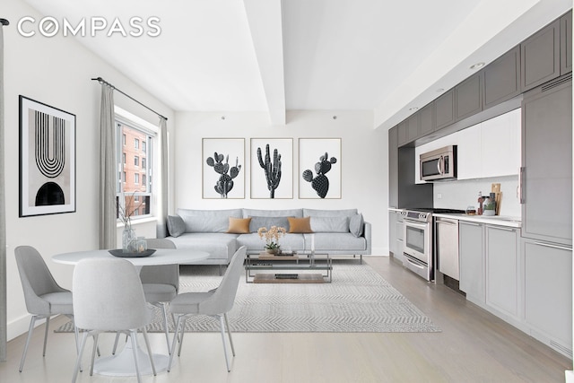 living room featuring beam ceiling, light wood-style floors, and baseboards