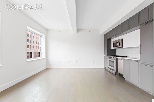 kitchen with stainless steel appliances, light wood finished floors, beam ceiling, baseboards, and light countertops
