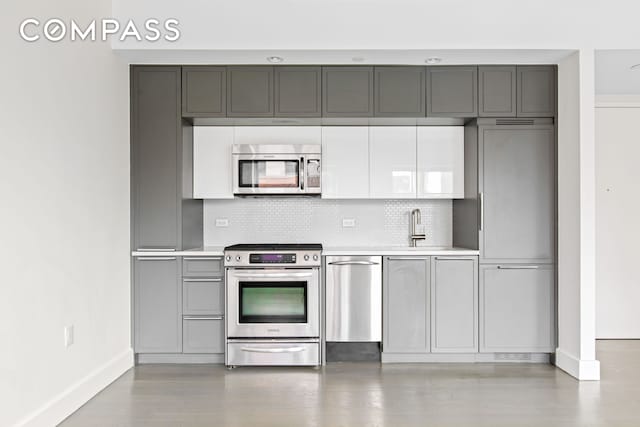 kitchen featuring stainless steel appliances, a sink, light countertops, baseboards, and gray cabinetry