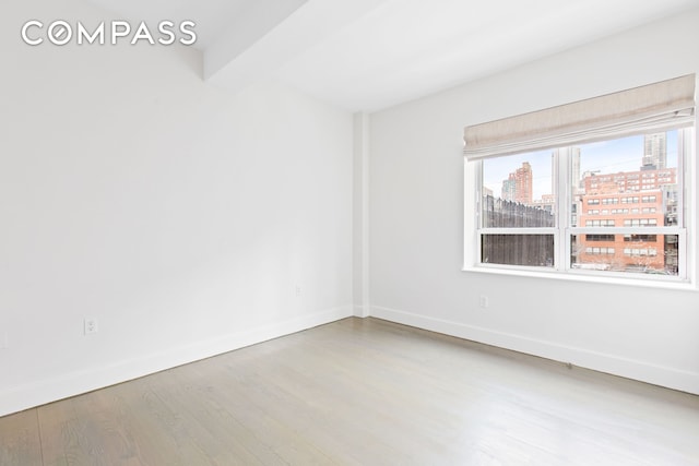 empty room featuring wood finished floors, a view of city, and baseboards