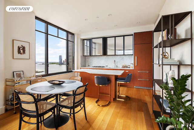 dining area with light wood-style flooring, bar with sink, and a water view