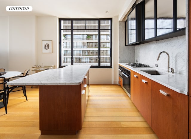 kitchen featuring a sink, black oven, healthy amount of natural light, and light wood-style flooring