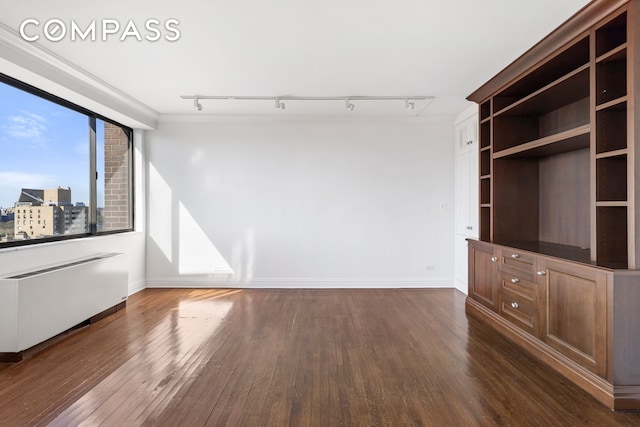 unfurnished living room with track lighting, dark wood finished floors, baseboards, and crown molding