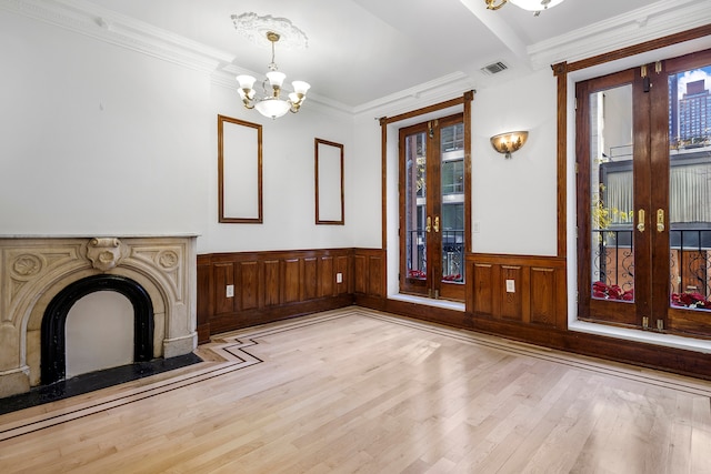 245 E 52nd St, New York City, NY 10022 - unfurnished living room with french doors, a chandelier, light wood-style flooring, wainscoting, and a high end fireplace