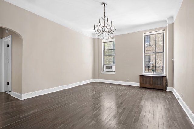 empty room featuring arched walkways, dark wood finished floors, baseboards, a chandelier, and crown molding