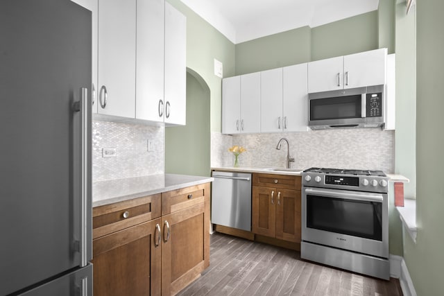 kitchen with stainless steel appliances, light countertops, a sink, wood finished floors, and white cabinets
