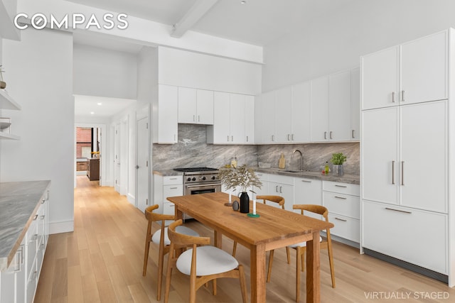 kitchen featuring a sink, light wood-style floors, decorative backsplash, a towering ceiling, and white cabinets
