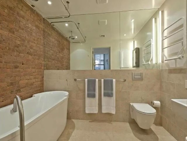 full bathroom with a soaking tub, toilet, tile walls, and brick wall